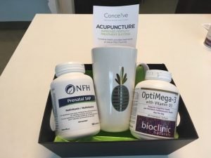 A basket with a mug with an image of a pineapple, a bottle of Prenatal SAP, a bottle of optimega-3 with vitamin D 3 and a tag with the text: Acupuncture improves fertility treatment success. Logo: Conceive.