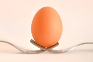 An egg balances on two intertwined forks.
