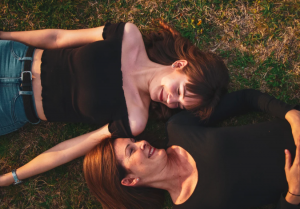 Two people of different generations lying on the grass and smiling at each other.