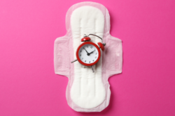 White menstrual pad with a small red clock sitting on it, pink background in photo