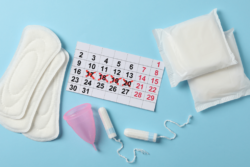 An open menstrual pad, packaged menstrual pad, tampon and menstruation cup with a calendar with 4 days crossed off in red pen